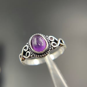 Könnte beinhalten: Ein silberner Ring mit einem ovalen Amethyst-Edelstein, der in einem dekorativen Filigranmuster gefasst ist.