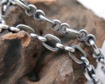 May include: Close-up of a silver chain necklace with oval and round links. The necklace is displayed on a piece of weathered wood against a white background. The chain has a vintage, industrial aesthetic.