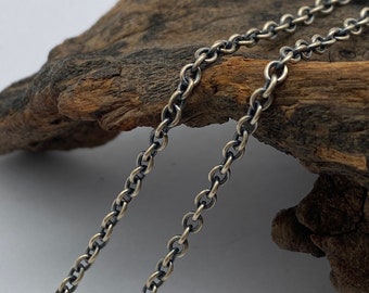 May include: A silver chain necklace with a dark oxidised finish. The chain is made of small, round links and is draped over a piece of driftwood.