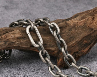 May include: A silver chain necklace with a thick, oval-shaped link design. The chain is lying on a piece of weathered wood.