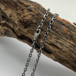 May include: A silver chain necklace with a lobster clasp. The chain is made of small, linked ovals.