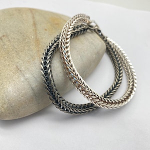 Op de afbeelding: Twee zilveren creolen met een gevlochten ontwerp. Een oorring is zilver en de andere is geoxideerd zilver.