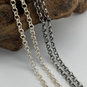May include: Three silver chains of different lengths, two are shiny and one is oxidised, lying on a piece of driftwood.