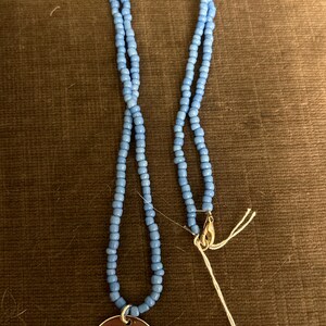 Puede incluir: Un collar de cuentas azul claro con un dije de plata que dice "Ohana means family".