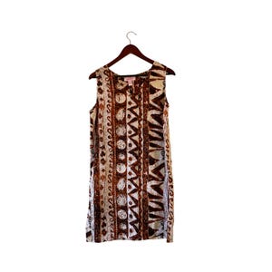 May include: A sleeveless knee-length dress featuring a repeating vertical pattern in shades of brown, tan, and white. The design includes circular motifs, jagged geometric shapes, and wavy lines. The garment is displayed on a brown wooden hanger.