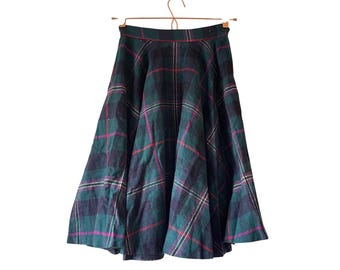 May include: A green, navy, and magenta plaid skirt hangs on a wooden hanger. The skirt has a full, flared shape and a classic tartan pattern. The fabric appears to be a medium-weight material.