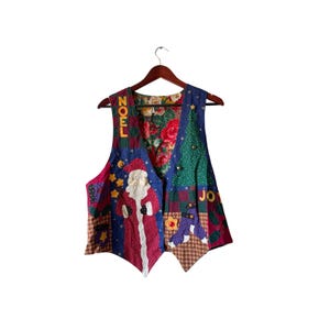 May include: A sleeveless waistcoat featuring a patchwork design with Christmas motifs including a Santa Claus figure, a green Christmas tree, and the words NOEL and JOY. The garment has a dark blue base with red, brown, and green accents and a floral lining.