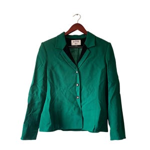 May include: A green blazer with a black collar and three buttons. The blazer is hanging on a wooden hanger. The label reads "KASPER A.S.L."