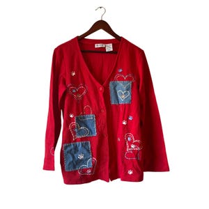 May include: Red cardigan with long sleeves, a V-neck, and button closure. The sweater features embroidered hearts, paw prints, and denim patches with heart designs. The brand label is visible at the top.