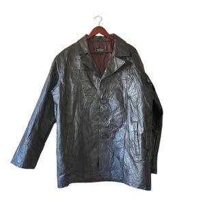 May include: A black leather jacket with a button-up front and a collared neckline. The jacket is hanging on a wooden hanger. The jacket has a textured appearance and a dark brown interior lining.