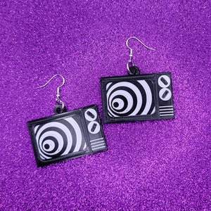 May include: A pair of black and white television earrings. The earrings are shaped like a vintage television with a hypnotic spiral pattern on the screen.