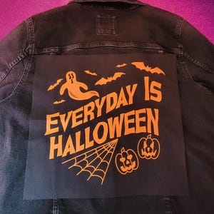 May include: Black denim jacket with an orange graphic that reads "EVERYDAY IS HALLOWEEN." The design includes a ghost, bats, a spider web, and jack-o'-lanterns. The jacket is a dark wash denim.