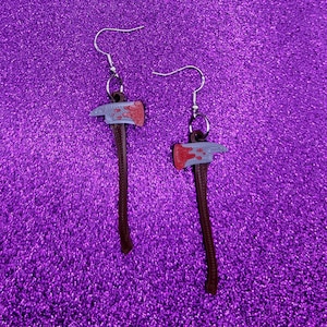 May include: A pair of silver earrings with a bloody axe charm. The axe is painted silver with red accents.