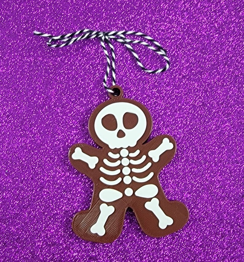 May include: A brown gingerbread man ornament with a white skeleton design. The ornament has a white string attached to the top.