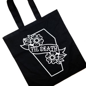 May include: Black tote bag with a white graphic of a coffin with flowers and the text "Til Death".