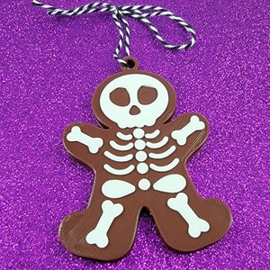 May include: A brown gingerbread man ornament with a white skeleton design. The ornament has a string attached for hanging.