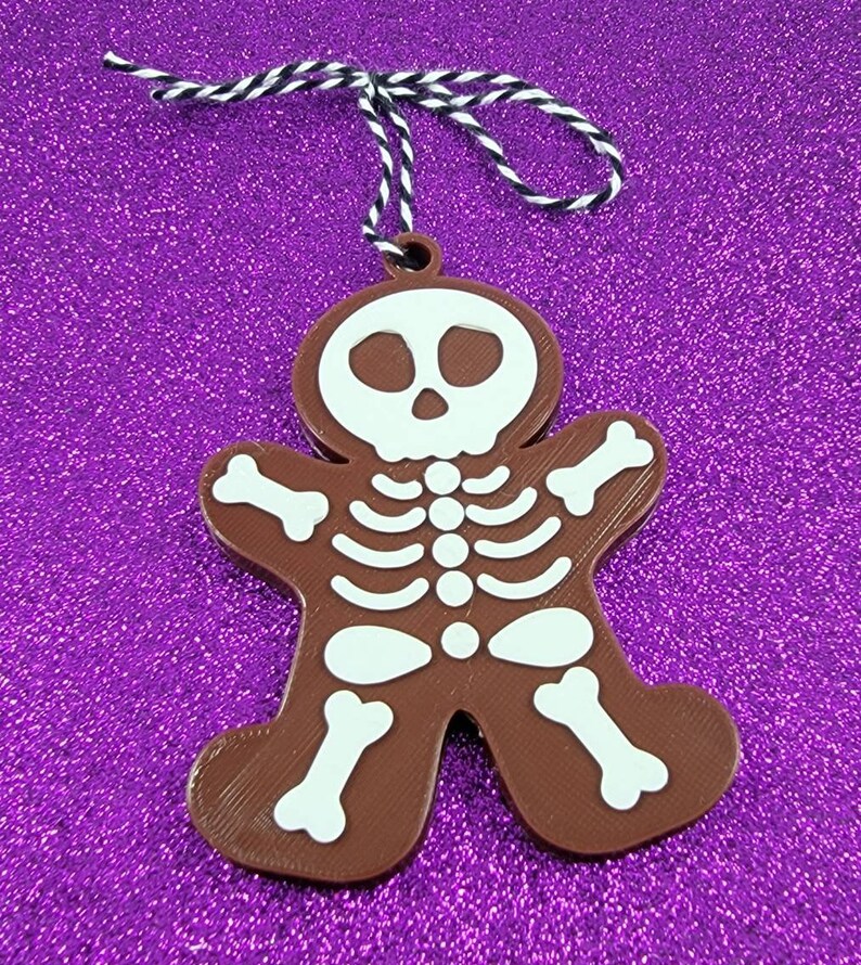 May include: A brown gingerbread man ornament with a white skeleton design. The ornament has a string attached for hanging.