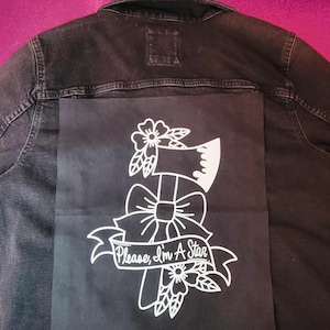 May include: Black denim jacket with a large black patch on the back. The patch features a white graphic of an axe, bow, and flowers, with the text "Please, I'm A Star" in a banner.