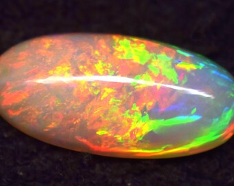 May include: An oval-shaped opal gemstone with a milky white base and vibrant internal play-of-color. The gemstone displays flashes of red, orange, yellow, green, and blue, creating a dynamic and iridescent effect. The opal is set against a dark background.