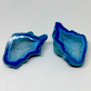 May include: Two blue agate geode halves with a white crystal interior. The geode halves are a light blue colour with a darker blue band around the edge.