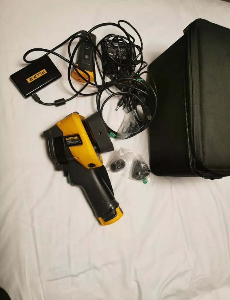 May include: A yellow and black handheld thermal imaging camera with a black carrying case, a black power adapter, and a black battery pack. The camera has a black handle and a yellow trigger. The camera is labeled "FLUKE" and "TI300".
