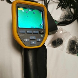 May include: A yellow and black Fluke thermal imaging camera with a 23.5&deg;C temperature reading on the screen. The camera has a black handle and a black strap.
