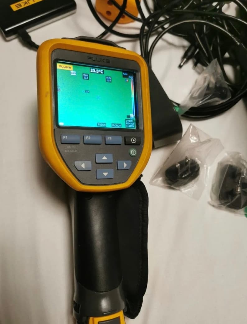 May include: A yellow and black Fluke thermal imaging camera with a 23.5&deg;C temperature reading on the screen. The camera has a black handle and a black strap.