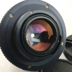 K&ouml;nnte beinhalten: Ein schwarzes Kameraobjektiv mit einem silbernen Ring am Rand. Das Objektiv hat eine gro&szlig;e Blende und ein klares Glaselement.