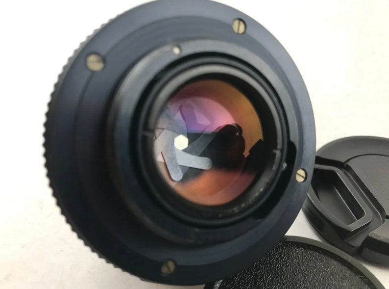 K&ouml;nnte beinhalten: Ein schwarzes Kameraobjektiv mit einem silbernen Ring am Rand. Das Objektiv hat eine gro&szlig;e Blende und ein klares Glaselement.