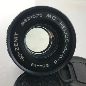 K&ouml;nnte beinhalten: Ein schwarzes Kameraobjektiv mit dem Text "MC HELIOS-44M 9-WM 58mm f:2 ZENIT-80f M52x0,75" um den Rand gedruckt.