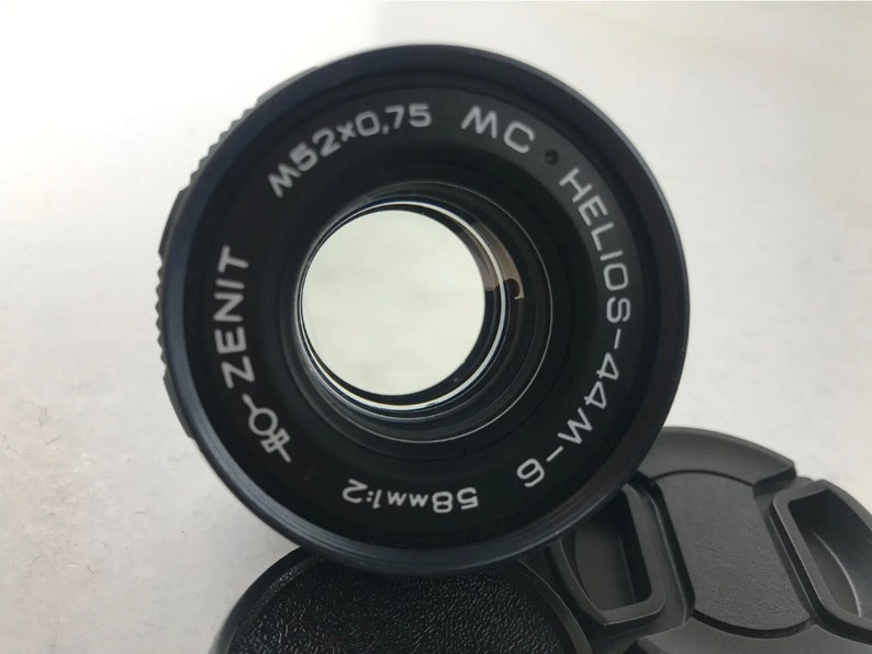 K&ouml;nnte beinhalten: Ein schwarzes Kameraobjektiv mit dem Text "MC HELIOS-44M 9-WM 58mm f:2 ZENIT-80f M52x0,75" um den Rand gedruckt.