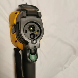May include: A yellow and black thermal imaging camera with a green button and a black strap. The camera has a lens cover that is open, revealing the lens and a laser pointer.