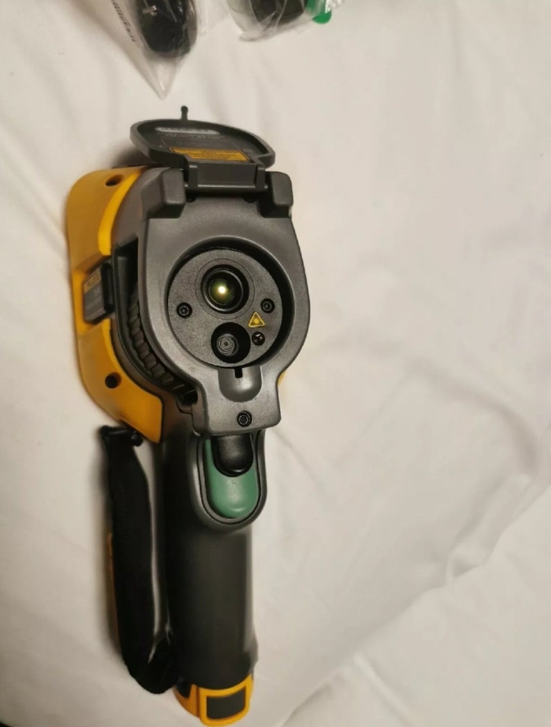 May include: A yellow and black thermal imaging camera with a green button and a black strap. The camera has a lens cover that is open, revealing the lens and a laser pointer.