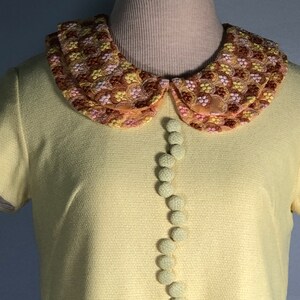May include: A yellow short-sleeved dress with a large embroidered collar and a row of fabric buttons down the front.
