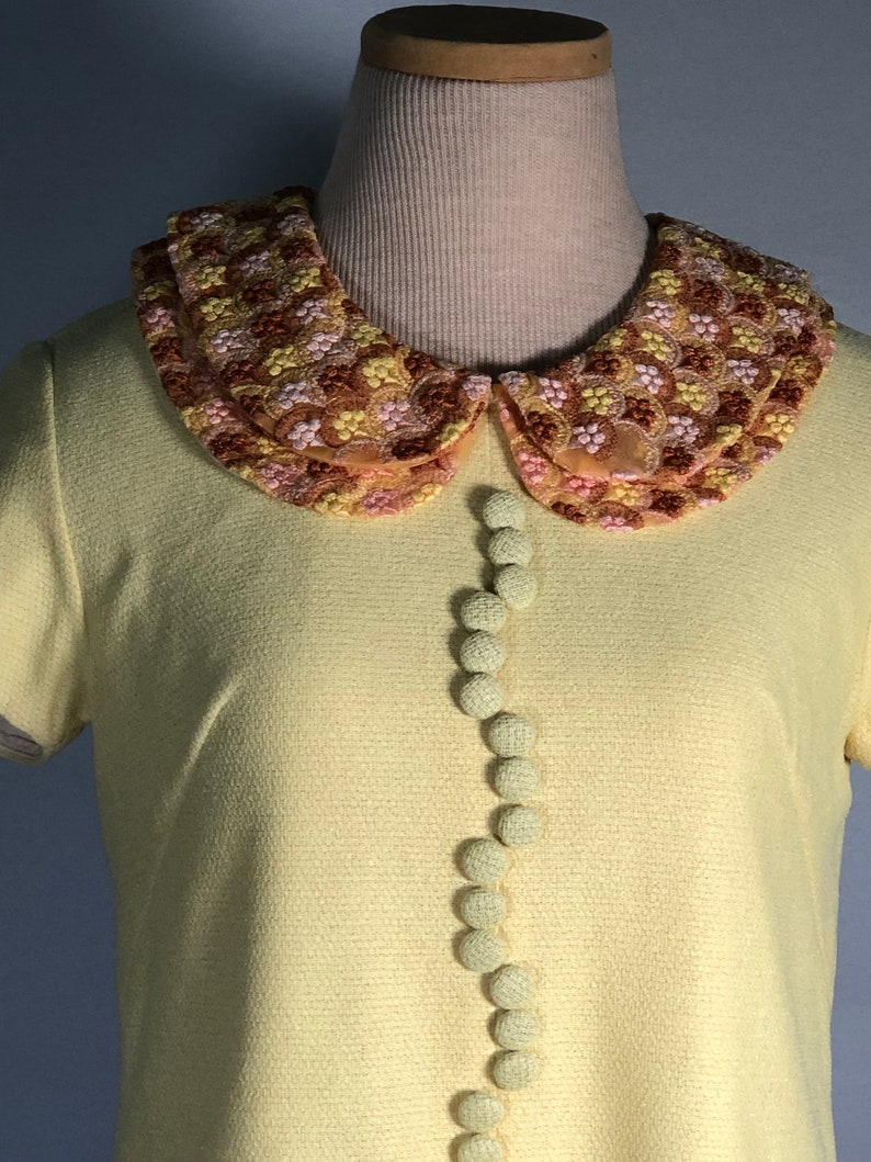 May include: A yellow short-sleeved dress with a large embroidered collar and a row of fabric buttons down the front.