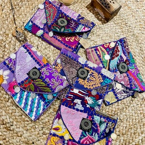 Peut inclure: Six porte-monnaie en tissu patchwork coloré avec des détails brodés et des accents métalliques argentés. Les porte-monnaie sont disposés sur une surface en paille tissée.