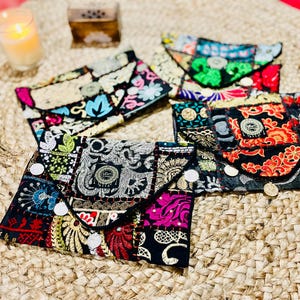 Peut inclure: Cinq pochettes en tissu patchwork colorées avec des détails brodés et des boutons décoratifs. Les pochettes sont disposées en rangée sur une surface en paille tissée.
