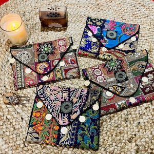 Peut inclure: Cinq pochettes en tissu colorées avec des motifs brodés et des accents dorés. Les pochettes ont une fermeture à rabat et sont décorées de différents motifs et embellissements.