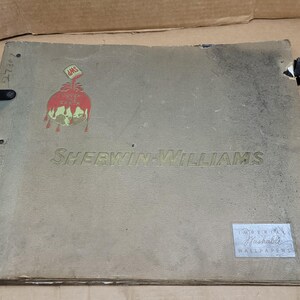 May include: Vintage Sherwin-Williams wallpaper catalog. The cover is a faded gray with the company name in embossed lettering. A colorful logo of a paint can spilling paint is on the cover. Includes black metal clasps.
