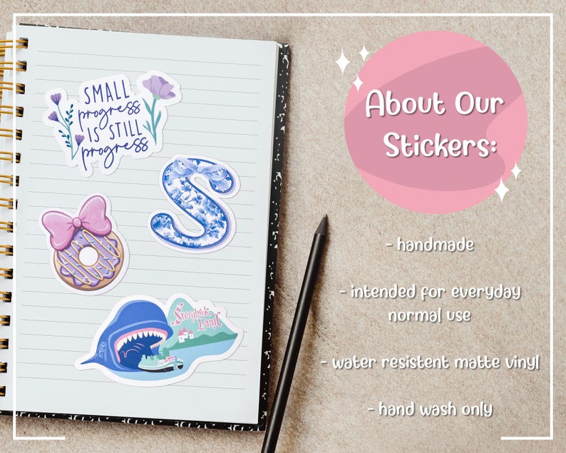 May include: A spiral-bound notebook with several colorful stickers. The stickers include a floral design with the text "Small progress is still progress", a blue letter "S", and a donut with a pink bow.