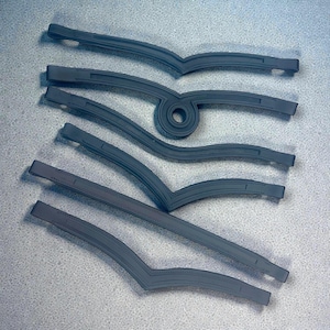 May include: A collection of gray, curved leather browbands for equestrian use. The browbands have a V-shape design with stitched detailing and a loop. The pieces are arranged on a light gray surface.