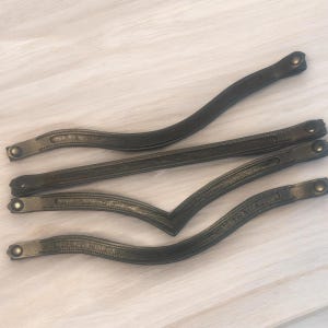 May include: Four dark green leather straps with gold-toned metal buckles. The straps are arranged in a criss-cross pattern.