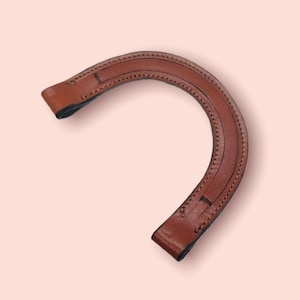 May include: A brown leather handle with a stitched design. The handle is curved and has a rounded shape.