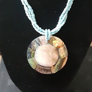 May include: A multi-strand necklace made of light blue beads with a large, round, iridescent shell pendant.