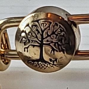 May include: Gold bangle bracelet with a charm featuring a detailed tree design.