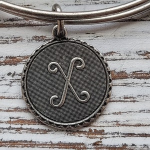 Op de afbeelding: Zilveren armband met een zilveren bedel met de letter X in een decoratief schrift.