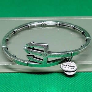 May include: Silver-toned bracelet with a trident charm and a small round tag that reads "VINTAGE SIXTY-SIX". The bracelet is on a green surface.
