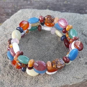 Op de afbeelding: Een kleurrijke kralen armband met een verscheidenheid aan stenen en kleuren, waaronder rood, oranje, geel, groen, blauw en wit.