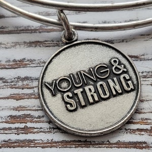 Puede incluir: Pulsera de plata con un dije de plata que dice "Young & Strong".