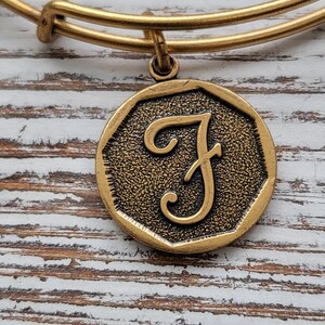 Puede incluir: Pulsera de charms de oro con un charm de oro en forma de letra F. El charm es octogonal y tiene una superficie texturizada.